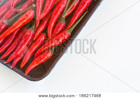 red hot chili peppers, popular spices concept - store packing of weighted red spicy peppers, peppers packing under plastic film in a dark disposable tray on white background - space for text