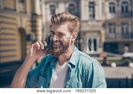 Stylish Young Red Bearded Man In Casual Jeans Outfit Is Talking On His Phone Outside. He Looks Fashi