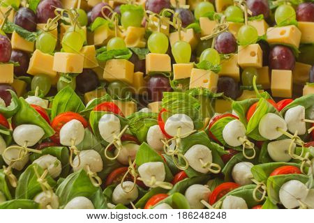 appetizer canape cheese with white and red grapes and tomato on bamboo skewers