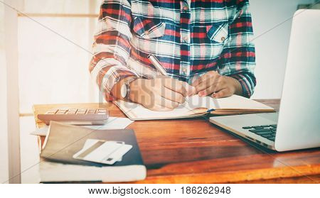 Finance and Accounting concept - Business asian female hands writing on income and expense accounts woman working at office and using computer and calculator. vintage colortone