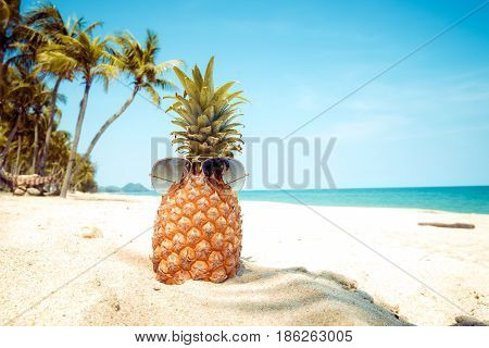 Hipster pineapple with sunglasses on a sandy beach with palm tree. concept of fashion in summer. vintage colortone filter effect