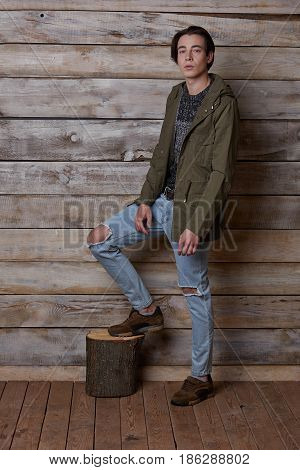 Handsome man wearing green jaket and torn jeans in wooden rural house interior