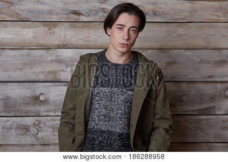 Handsome man wearing green jaket and torn jeans in wooden rural house interior