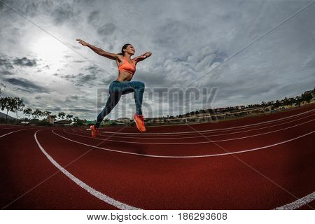 Female sprinter athlete starting a race on a tartan racetrack 