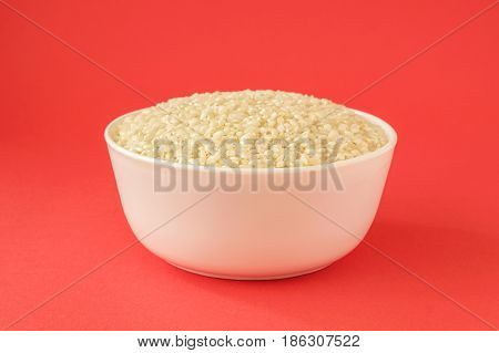 Raw medium grain rice in a bowl on red background. Gluten free grain