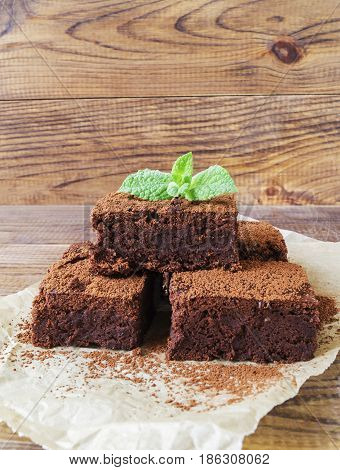 Sliced brownie decorated with cocoa powder and mint on paper on rustic wooden background selective focus vertical