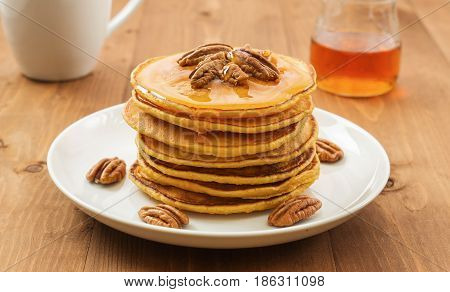 Vegan butternut squash puree pancakes on white plate with maple syrup and pecan nuts. Healthy gluten free breakfast on wooden table