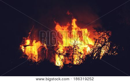 Arson or nature disaster - burning fire flame on wooden house roof. Big fire at night