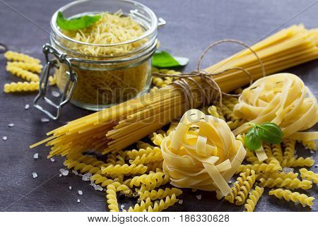 Different Types Of Pasta With Basil On The Kitchen Wooden Table. The Concept Of Italian Food.