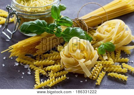 Different Types Of Pasta With Basil On The Kitchen Wooden Table. The Concept Of Italian Food.