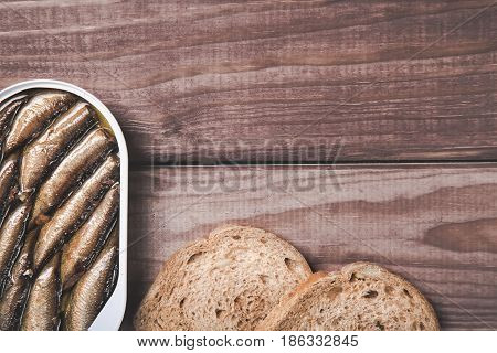 Tin can of sprats, sardines with bread pieces on wooden table. Top view and free space.