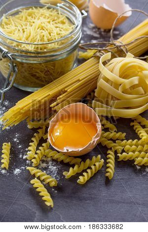 Various Types Of Pasta Spaghetti, Fusilli, Fettuccine And Raw Egg Yolk On A Kitchen Wooden Table. Co
