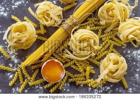 Different Kinds Of Pasta Spaghetti, Fusilli, Fettuccine And Raw Egg Yolk On The Kitchen Wooden Table
