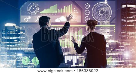 Two business people standing with back and working together with virtual screen