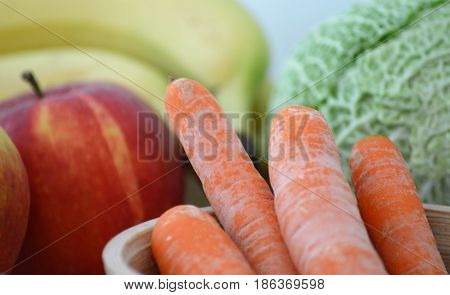 Raw carrots in a bamboo pot with apple, banana and cabbage in background