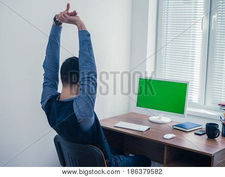 Tiredman office worker sitting at computer with Chromakey and stretching himself. Office concept with working environment. Back view