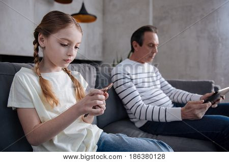 Apathetic towards real activities. Obsessed skillful cute girl sitting at home and using digital gadgets with grandfather while surfing the Internet and playing games