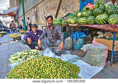 Bandar Abbas Hormozgan Province Iran - 16 april 2017: Two persian men sell vegetables and fruits sitting on the sidewalk under the open sky.