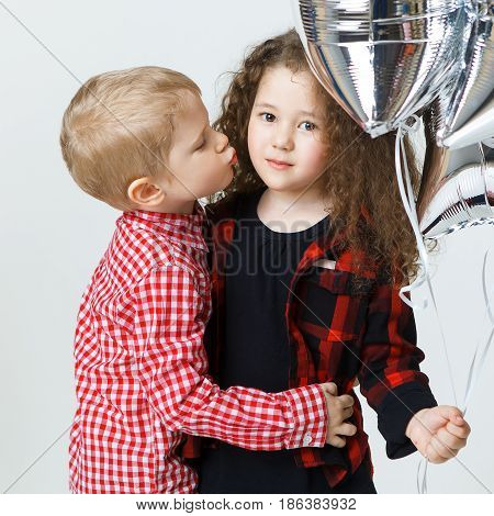 Little boy congatulate little curly girl, kiss, balloons. Fashion trendy clothes