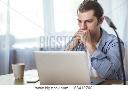 portrait of concetrated man with laptop at his home, window on background