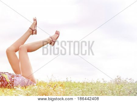 Low section of woman with feet up lying on grass against sky