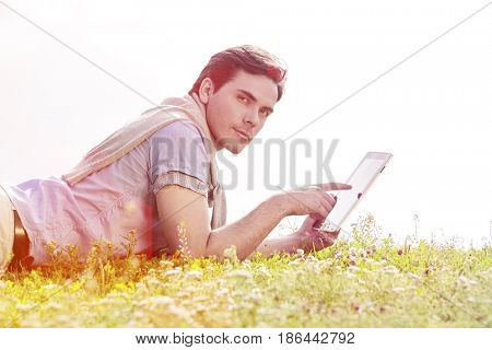 Side view of young man using digital tablet while lying on grass against clear sky