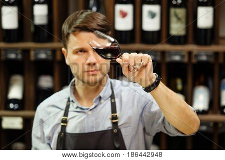 Bokal of red wine on background of male sommelier appreciating color, quality, flavor and sediments of drink. Professional degustation expert in winemaking.
