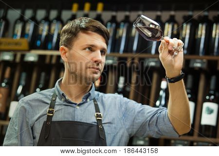 Bokal of red wine on background of male sommelier appreciating color, quality, flavor and sediments of drink. Professional degustation expert in winemaking.