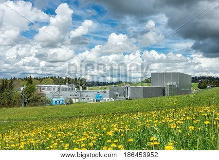 Factory in a rural scenic landscape on a flower meadow and nice sky. E cologically friendly cheese and milk dairy in Bavaria, Germany. Clean industry concept.