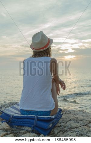 Lonesome girl watching the sunset / sunrise over sea / ocean horizon.