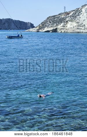 Man swimming in transparent sea water with boats and rocks on the background