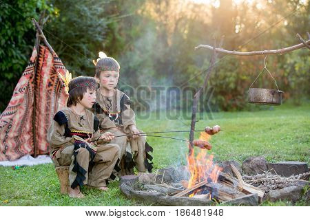 Cute Portrait Of Native American Boys With Costumes, Playing Outdoor Around Fire On Sunset