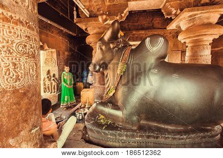 PATTADAKAL, INDIA - FEB 9, 2017: Young woman praying inside the Hindu temple with diety bull Nandi on February 9, 2017. UNESCO World Heritage site with stone carved structures of 7th-century