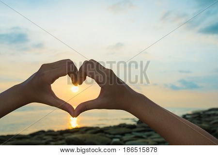 Female hands in the form of heart against sunlight in sunrise sky on beach morning time. Hands in shape of love heart Love concept.