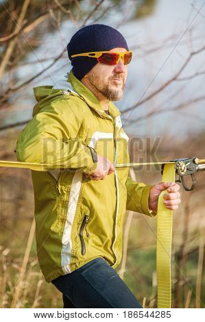 Close-up A man adjusts the slacklining of equipment before performing crazy slacklining tricks and walking on a slacklin in a park in the nature