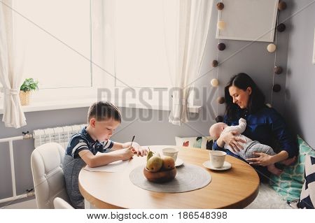 happy young mother having breakfast in kitchen with her baby daughter and kid son