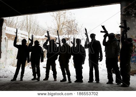 Eight unrecognizable young people with guns pose during lasertag game outdoor at winter day