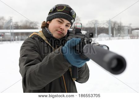 Boy with gun takes aim during lasertag game outdoor at winter day near railway station