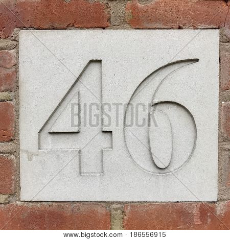 Number 46 forty six carved stone house number address sign screwed into painted white stone wall textured background