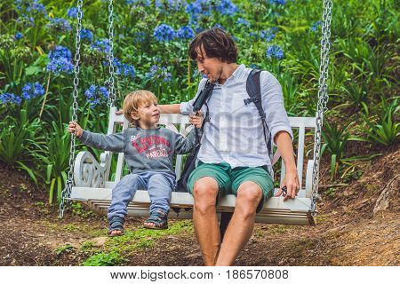 Father And Son Having Fun On Swings In A Flower Garden