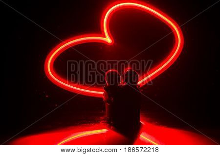 Two young lovers paint a heart on fire. Silhouette of couple and Love words on a dark background. Love concept