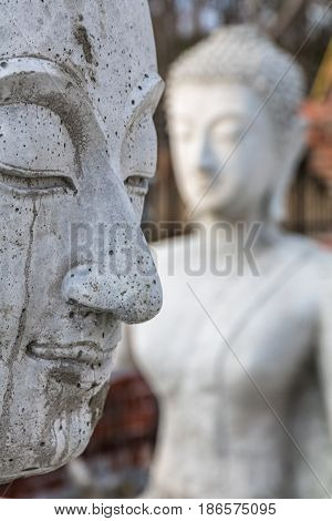 Close-up profile of a cement buddha statue with another buddha statue in soft focus behind it