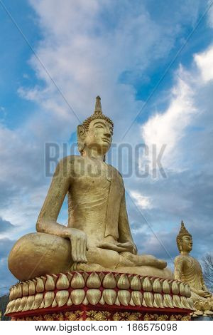 Large golden buddha statue shot from a low perspective with blue sky and clouds behind it