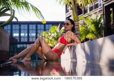 Woman sunbathing in bikini at tropical travel resort. Beautiful young woman sit in a shade at luxury hotel near the swimming pool.