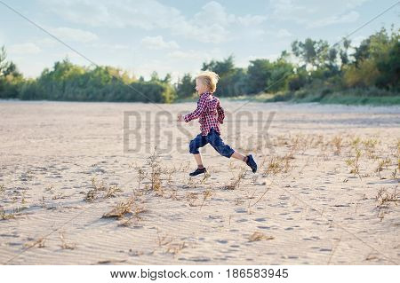 White Caucasian child kid boy playing running on sand beach dunes outdoors on summer day happy lifestyle childhood concept copyscpace for text