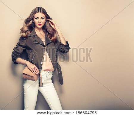 Young blond woman in brown jacket and white jeans. Girl posing on a beige background. Jewelry and hairstyle. Girl with brown handbag. Fashion photo