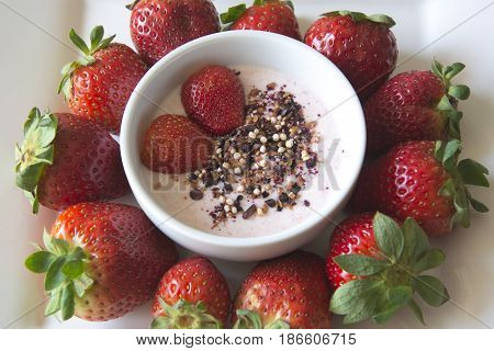Greek strawberry yoghurt in a bowl with a superfruit topping of dried blueberries, hibiscus, chia seeds and airy quinoa pops surrounded by delicious strawberries