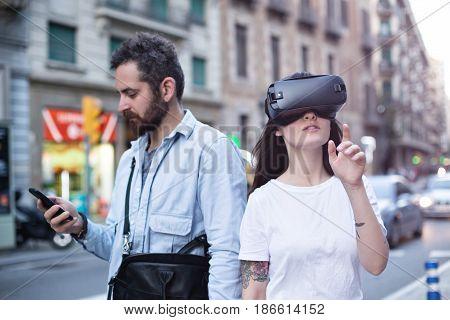 Authentic and trendy couple of millenials use augmented reality technology and VR headset in the busy city street