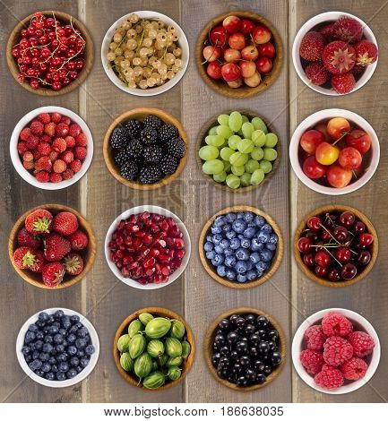 Collage of fruits and berries. Blueberries blackberries cherries grapes strawberries currants raspberries wild strawberries bilberries gooseberries and pomegranate. Collection of fruits and berries in a bowl. Top view.