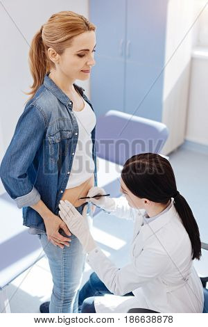 Do not move please. Positive female plastic surgeon looking at het patients stomach and putting some marks on it while doing her job